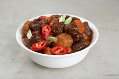 Delicious beef stew with carrots, chili peppers, green onions and potatoes on white textured table, closeup