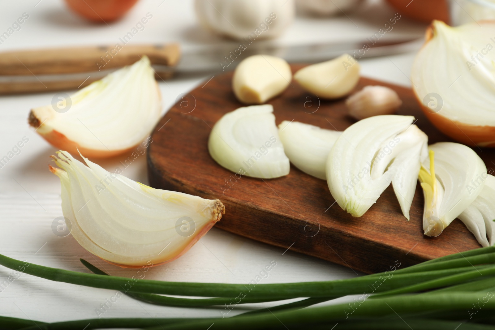 Photo of Board with cut onion and garlic on white wooden table