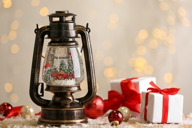 Photo of Beautiful snow globe in vintage lantern, gift boxes and Christmas decor on table against blurred festive lights