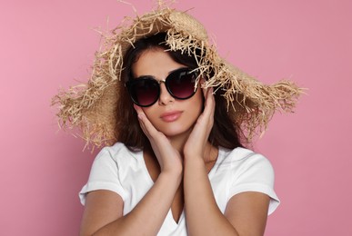 Beautiful woman with stylish straw hat and sunglasses on pink background