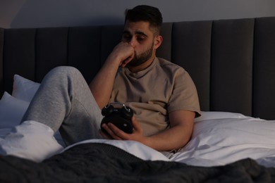 Frustrated man looking at alarm clock on bed