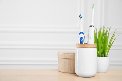 Photo of Electric toothbrushes in holder on wooden table. Space for text