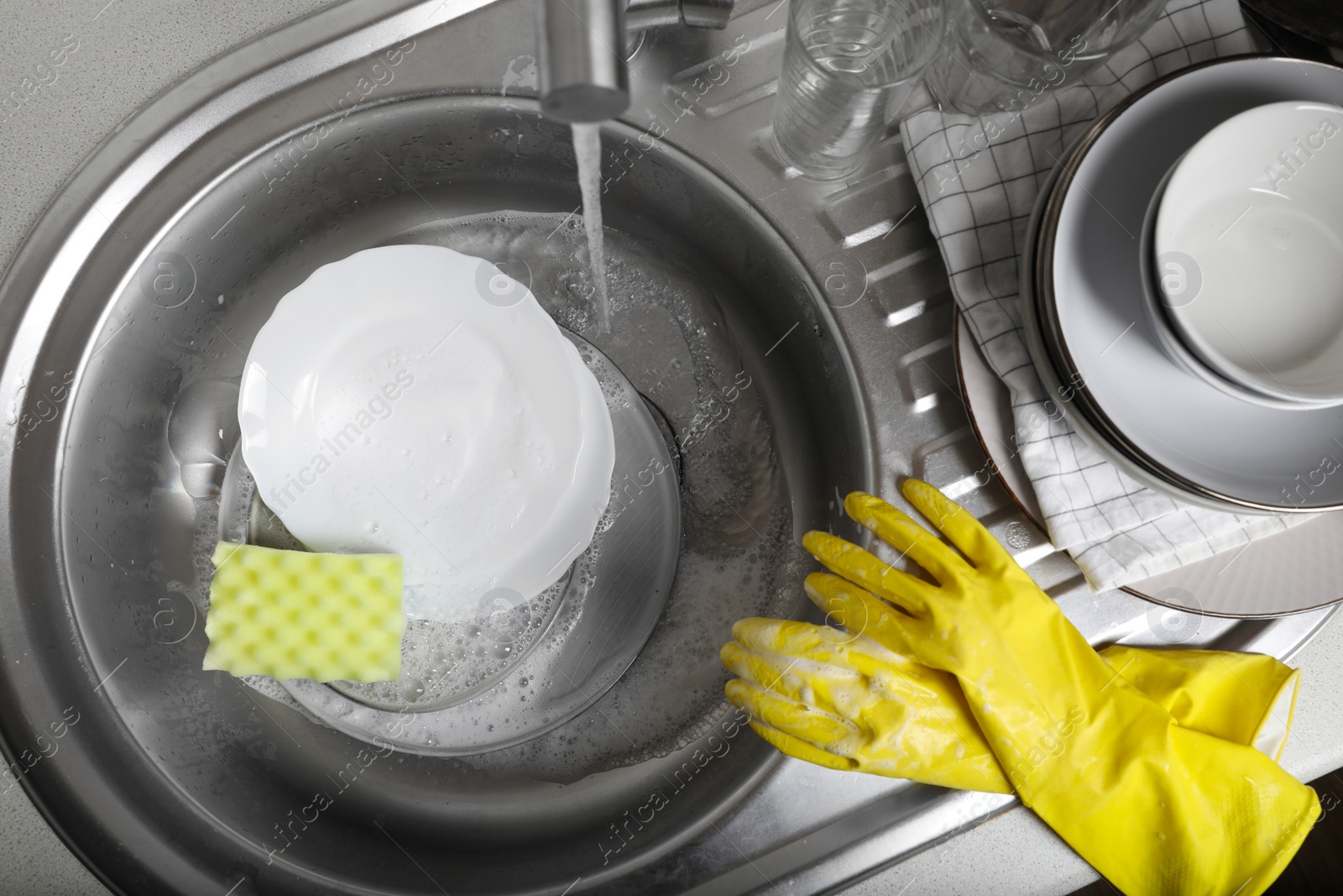 Photo of Washing plates, sponge and rubber gloves in kitchen sink, above view