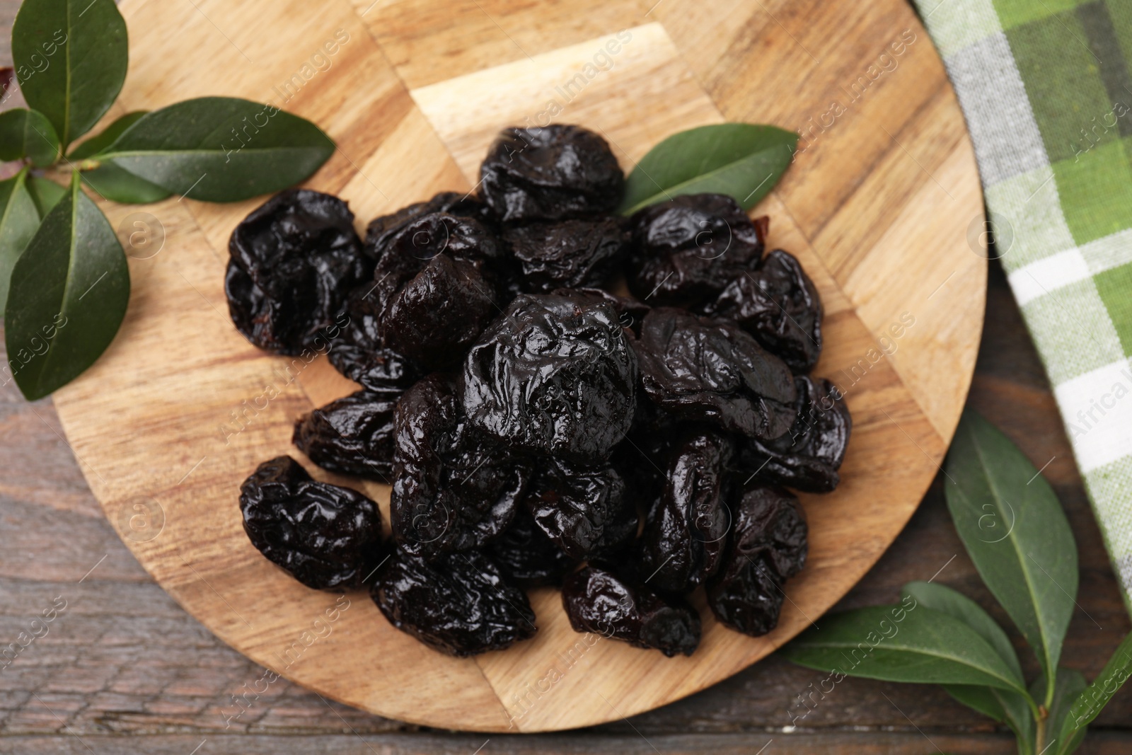 Photo of Tasty dried prunes and green leaves on wooden table, top view