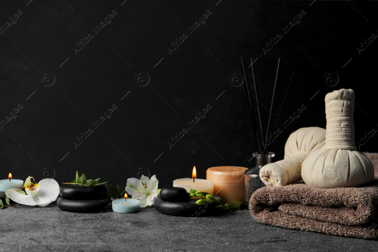 Photo of Beautiful spa composition with different care products and burning candles on dark grey table against black background. Space for text