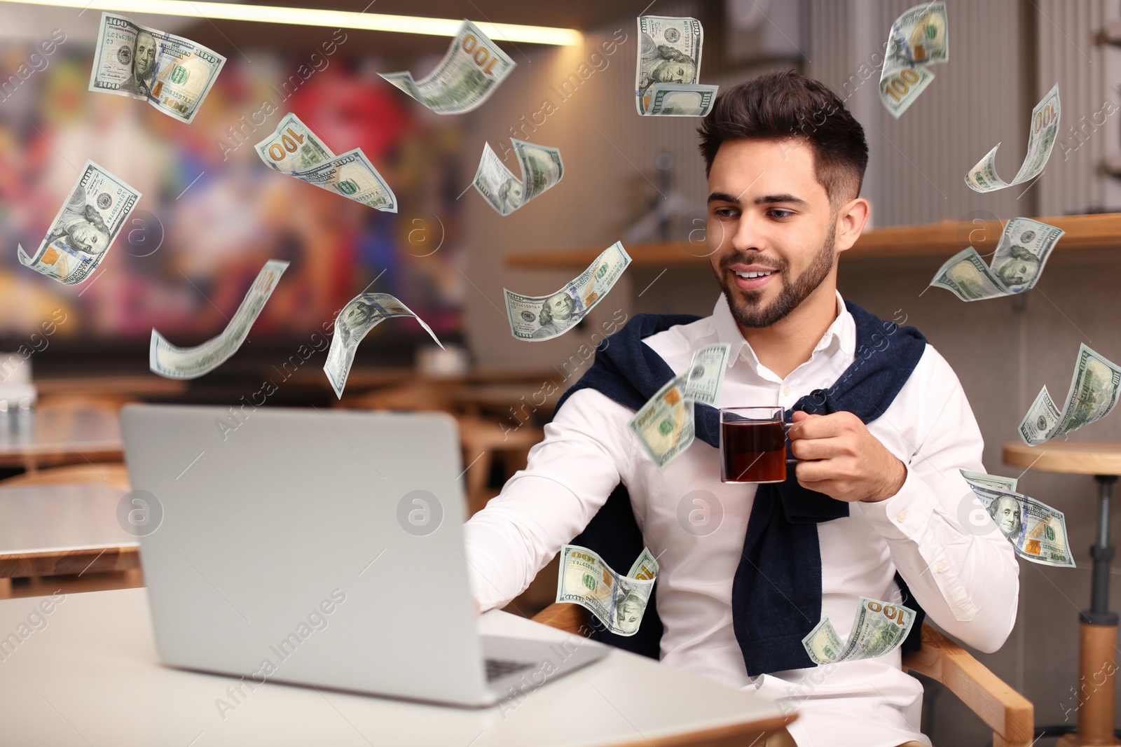 Image of Man with modern laptop and flying dollar banknotes at table indoors. People make money online