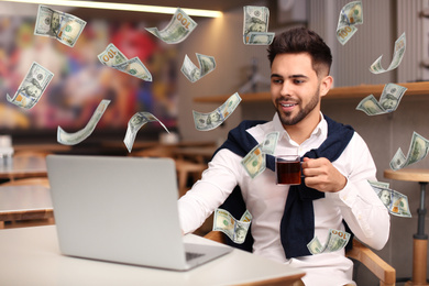 Man with modern laptop and flying dollar banknotes at table indoors. People make money online