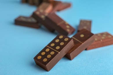 Photo of Falling wooden domino tiles on light blue background, closeup