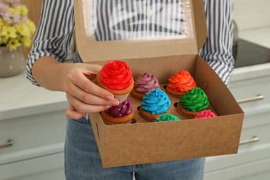 Photo of Woman holding box with delicious colorful cupcakes indoors, closeup