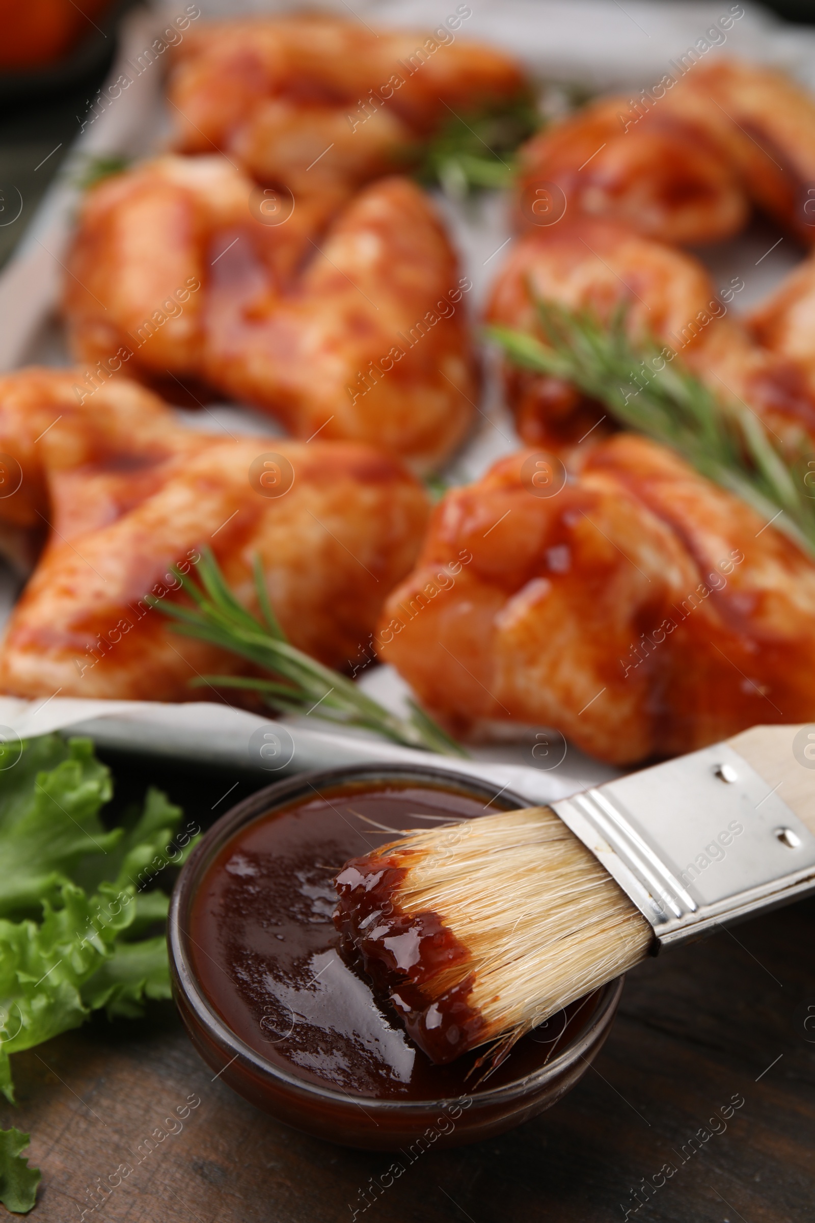 Photo of Fresh marinade, basting brush and raw marinated chicken wings on wooden table, closeup