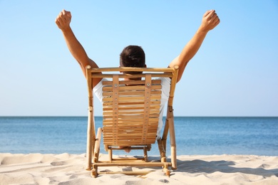 Photo of Young man relaxing in deck chair on sandy beach