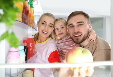 Photo of Happy family looking into refrigerator and choosing products in kitchen