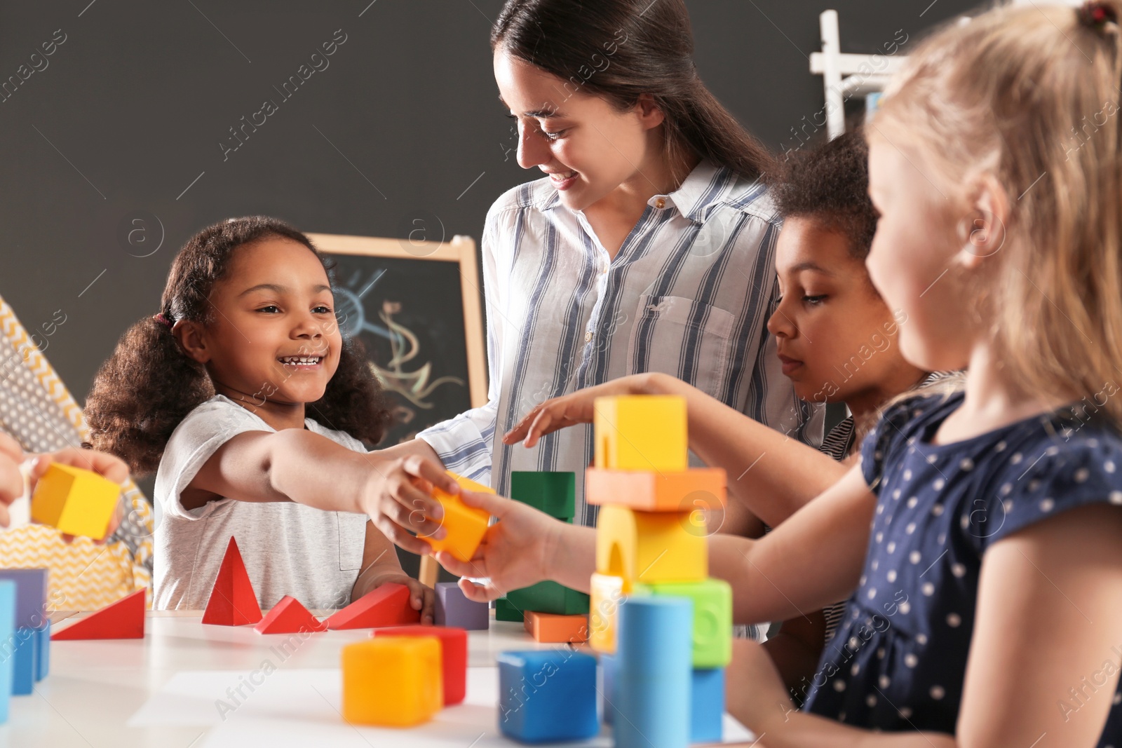 Photo of Cute little children and nursery teacher playing with building blocks in kindergarten. Indoor activity