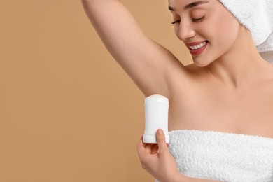 Beautiful woman applying deodorant on beige background, space for text