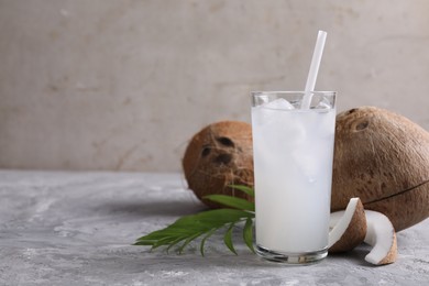 Photo of Glass of coconut water with ice cubes, palm leaf and nuts on grey table. Space for text