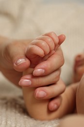 Photo of Mother holding hand of her newborn baby on beige blanket, closeup. Lovely family