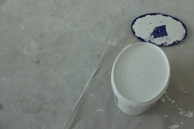 Photo of Open bucket with white paint on floor, above view. Space for text