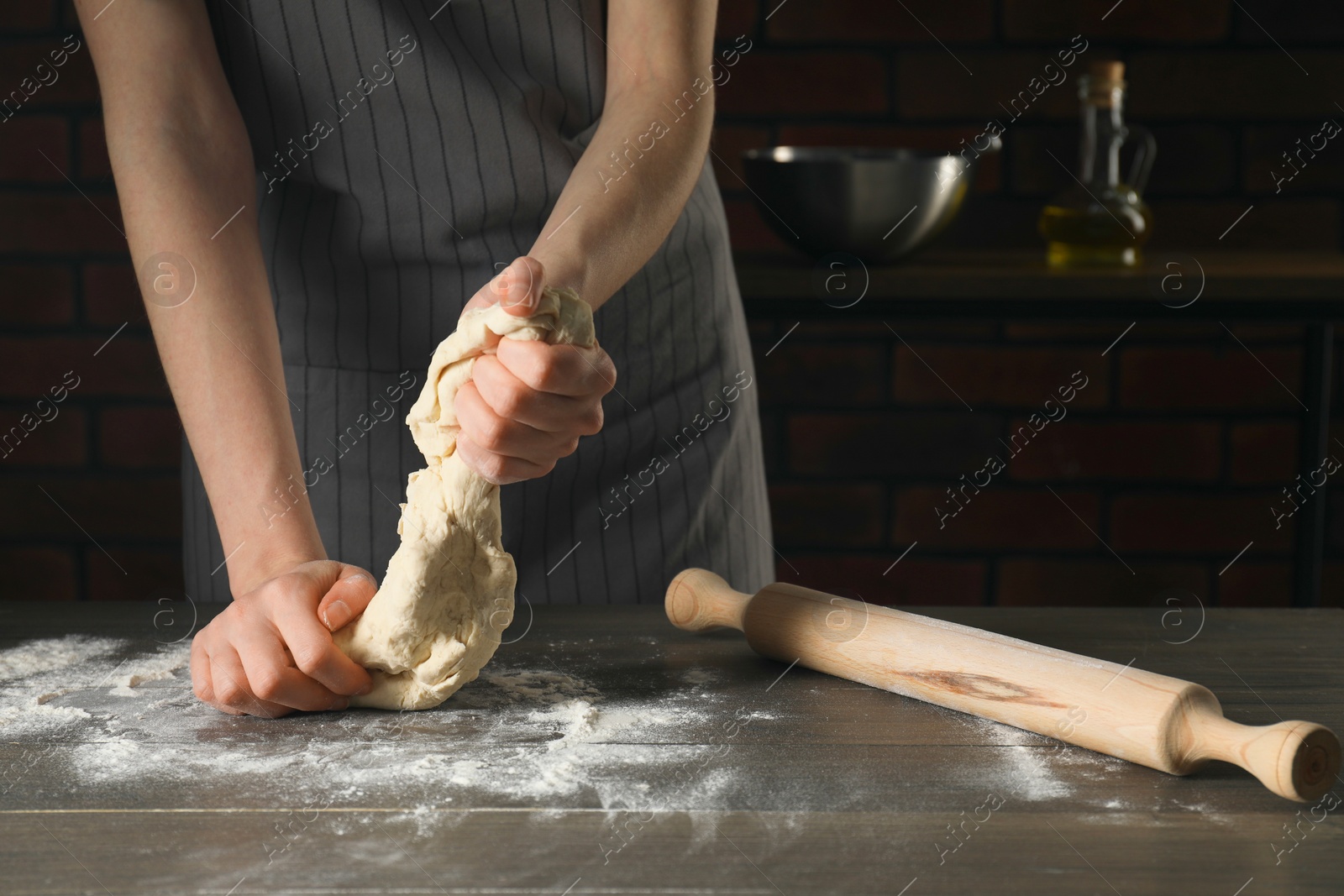 Photo of Making bread. Woman kneading dough at wooden table in kitchen, closeup