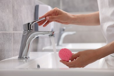 Photo of Young woman washing face sponge in bathroom, closeup