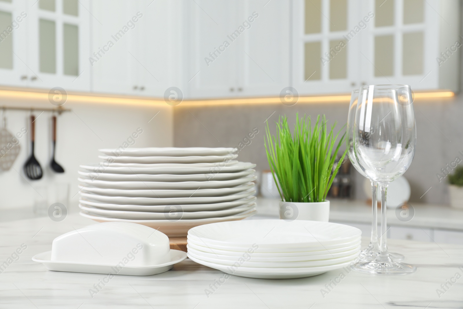 Photo of Clean plates, glasses, butter dish and floral decor on white marble table in kitchen