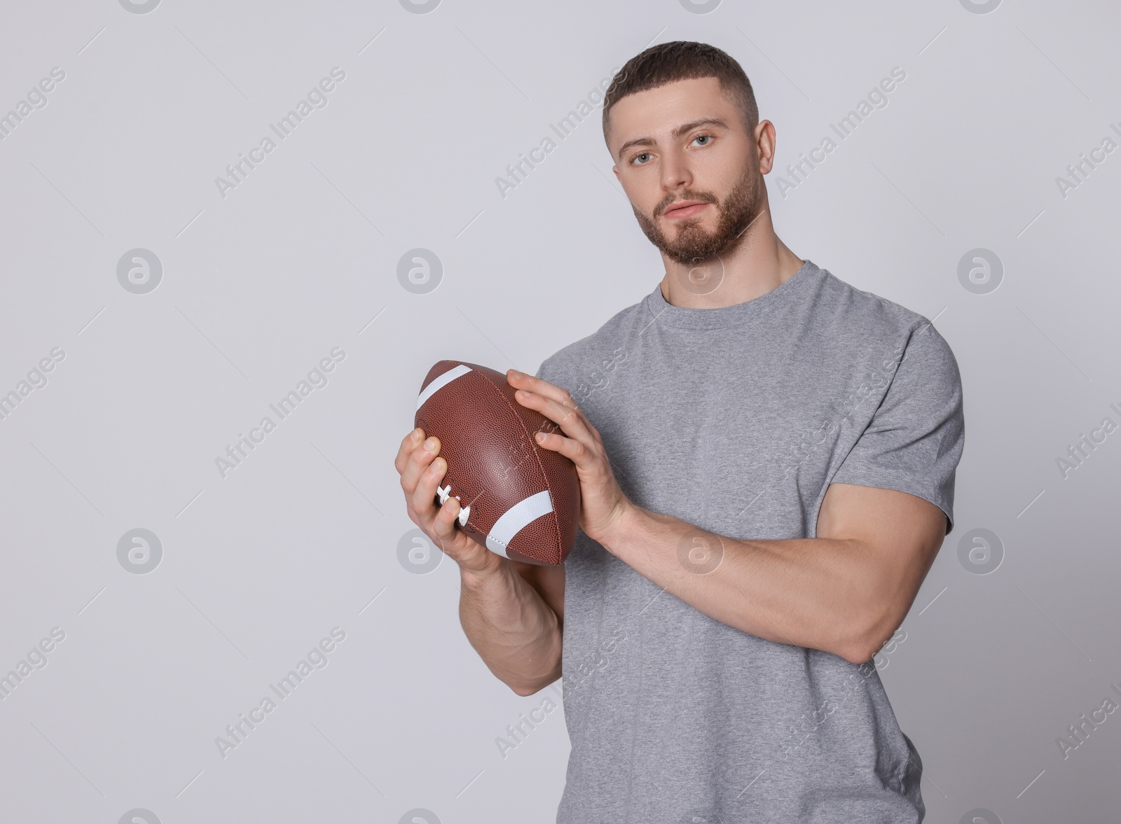 Photo of Athletic young man with American football ball on light grey background. Space for text