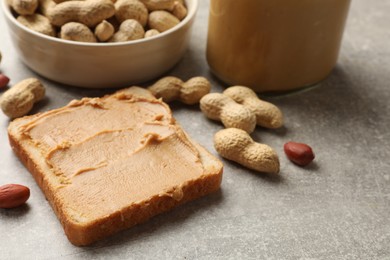 Photo of Tasty peanut butter sandwich and peanuts on gray table, closeup