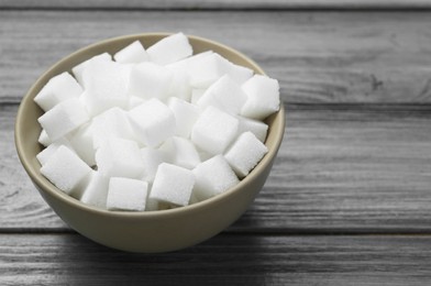 Photo of White sugar cubes in bowl on wooden table, closeup. Space for text