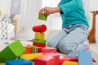 Photo of Cute little girl playing with colorful building blocks at home, closeup