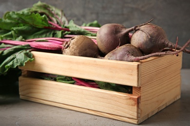 Photo of Wooden crate with fresh beets on table against grey background