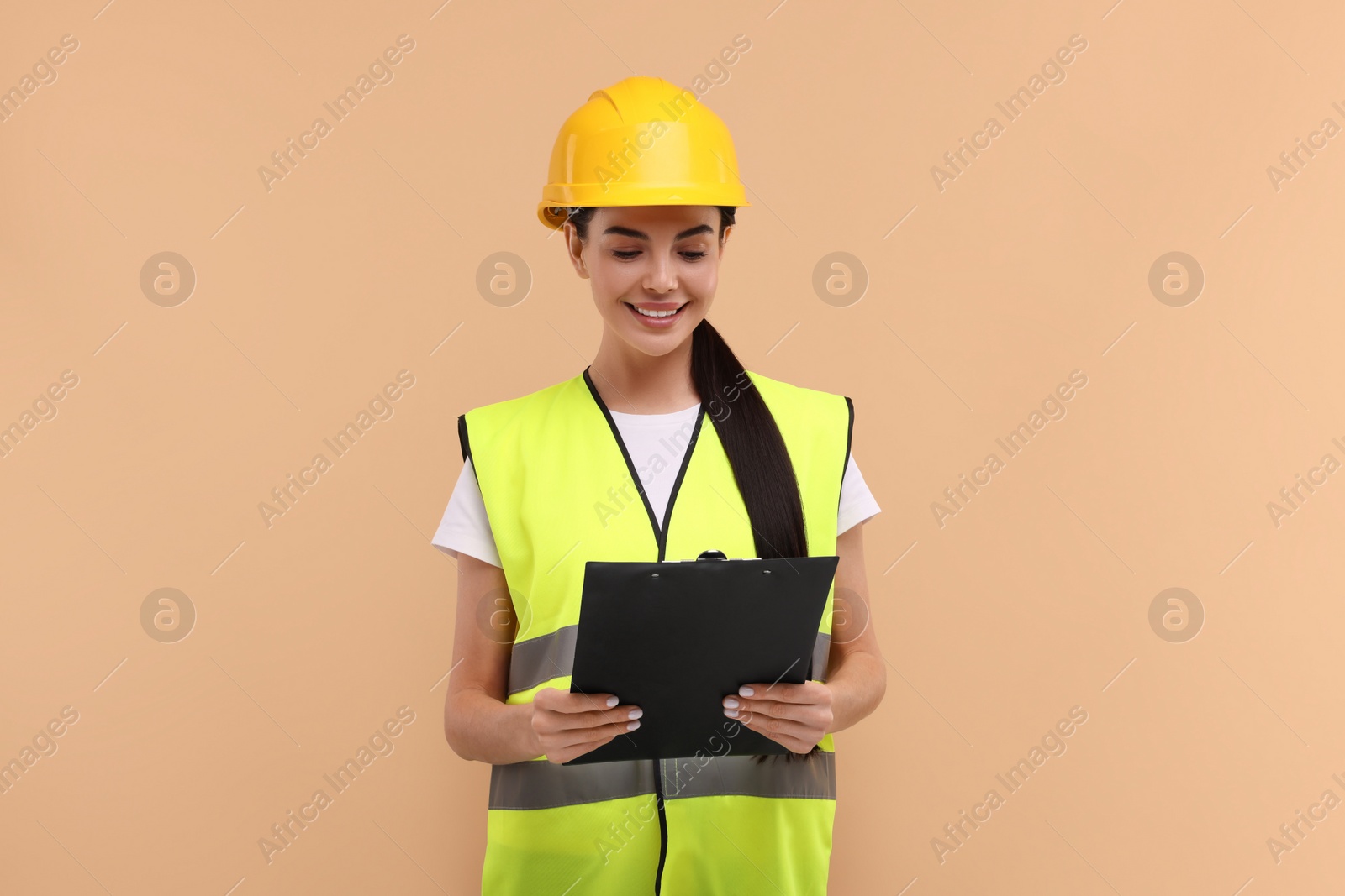 Photo of Engineer in hard hat holding clipboard on beige background