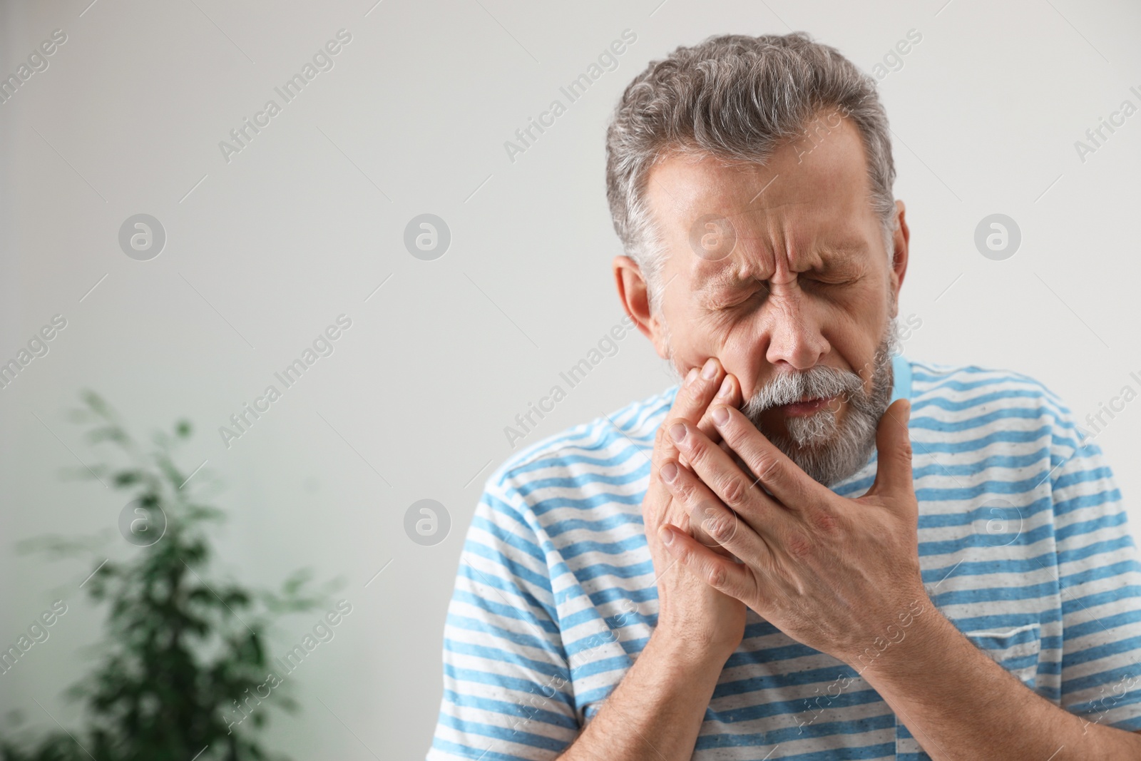 Photo of Mature man suffering from strong tooth pain at home, space for text