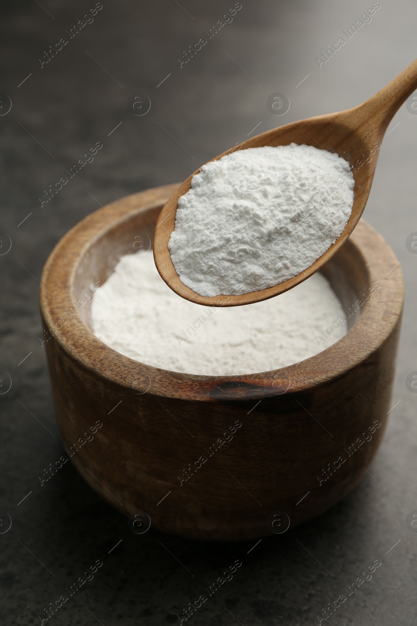 Photo of Baking powder in bowl and spoon on grey textured table, closeup