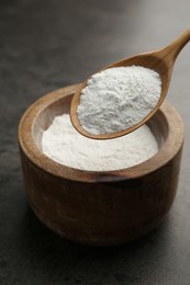 Baking powder in bowl and spoon on grey textured table, closeup