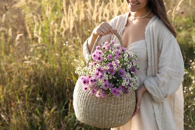 Photo of Woman holding wicker basket with beautiful wild flowers outdoors, closeup. Space for text