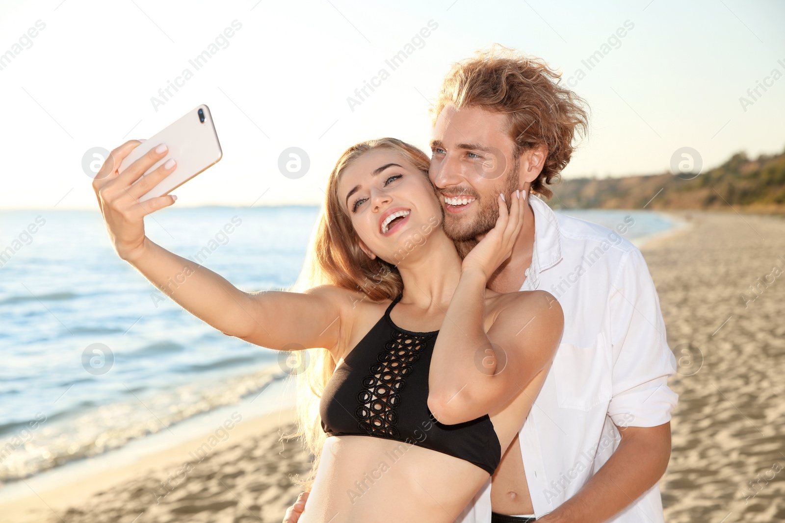 Photo of Happy young couple in beachwear taking selfie on seashore