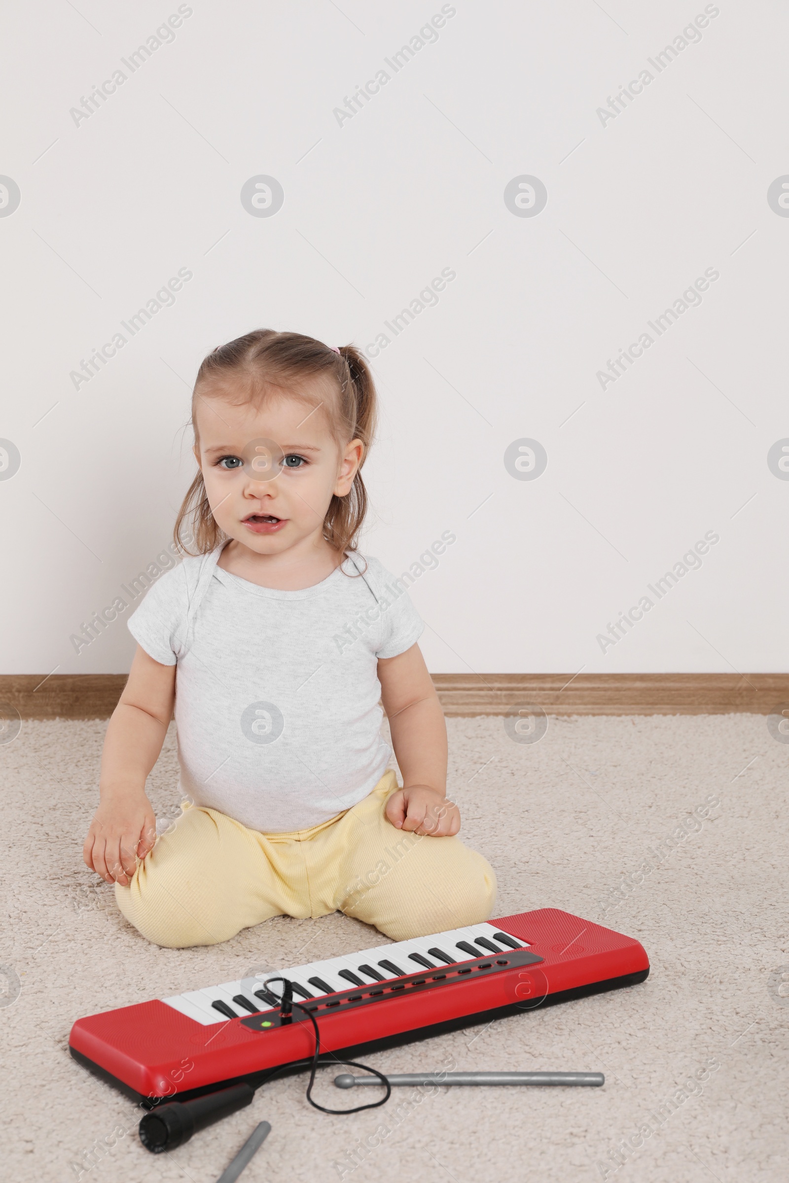 Photo of Cute little girl playing with toy piano at home