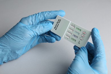 Doctor holding multi-drug screen test on light grey background, closeup