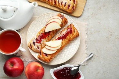 Photo of Fresh tasty puff pastry with jam and apples served on white textured table, flat lay. Space for text