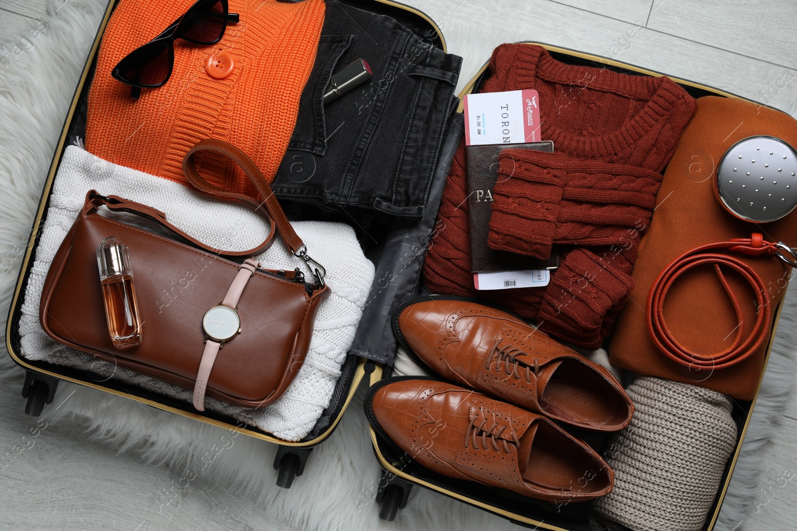 Photo of Open suitcase with folded clothes, accessories and shoes on floor, top view