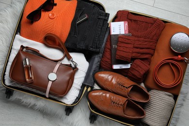 Photo of Open suitcase with folded clothes, accessories and shoes on floor, top view