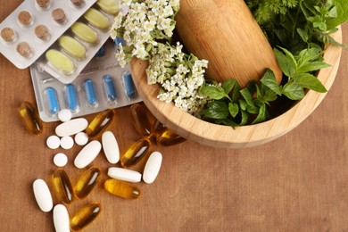 Mortar with fresh herbs and pills on wooden table, top view