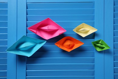 Photo of Colorful paper ships on blue wooden background, flat lay