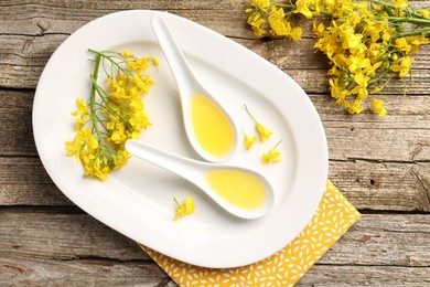 Photo of Rapeseed oil in gravy boats and beautiful yellow flowers on wooden table, top view