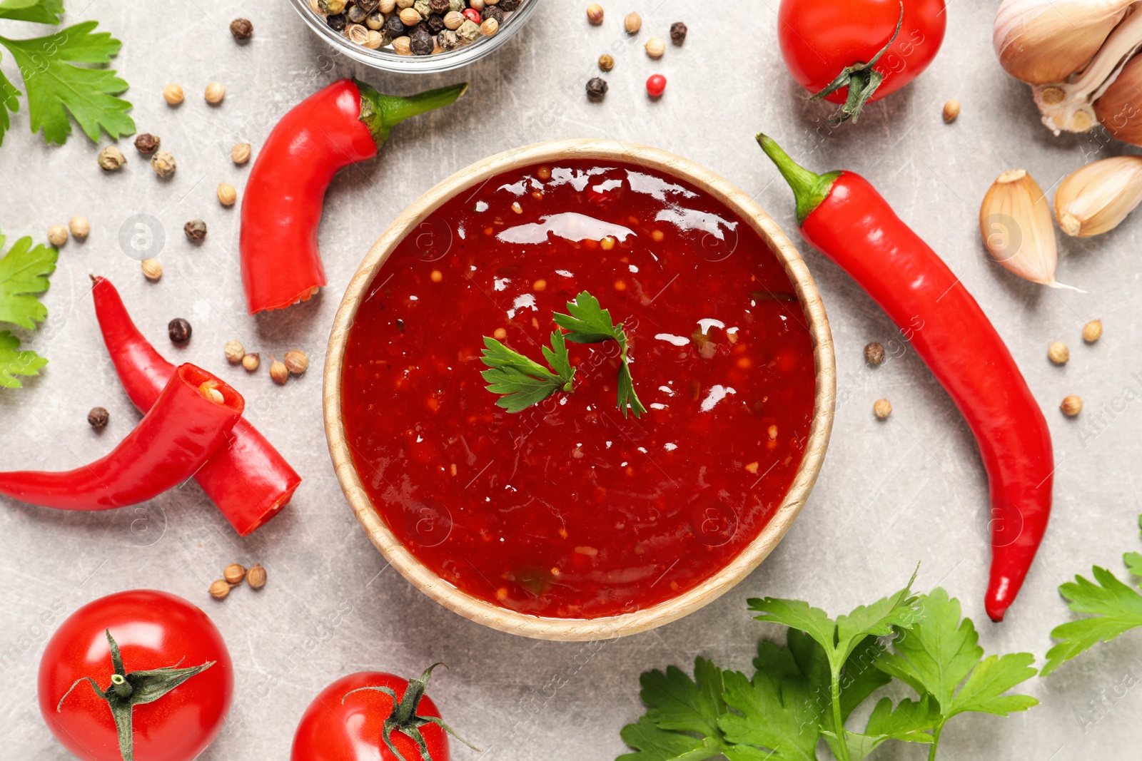 Photo of Spicy chili sauce and ingredients on light grey table, flat lay