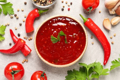 Spicy chili sauce and ingredients on light grey table, flat lay