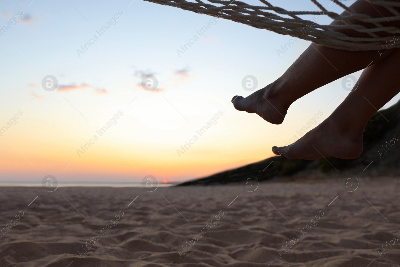 Photo of Young woman relaxing in hammock on beach at sunset, closeup