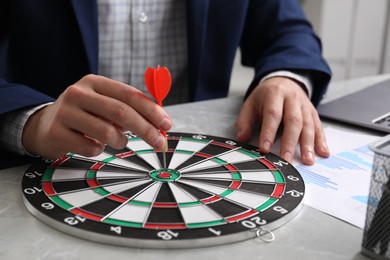 Business targeting concept. Man with dart aiming at dartboard at table, closeup