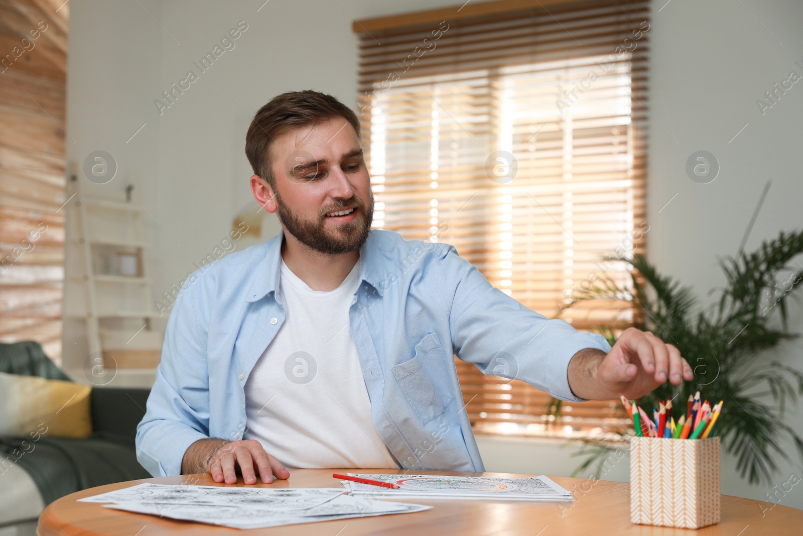 Photo of Young man coloring antistress picture at table indoors