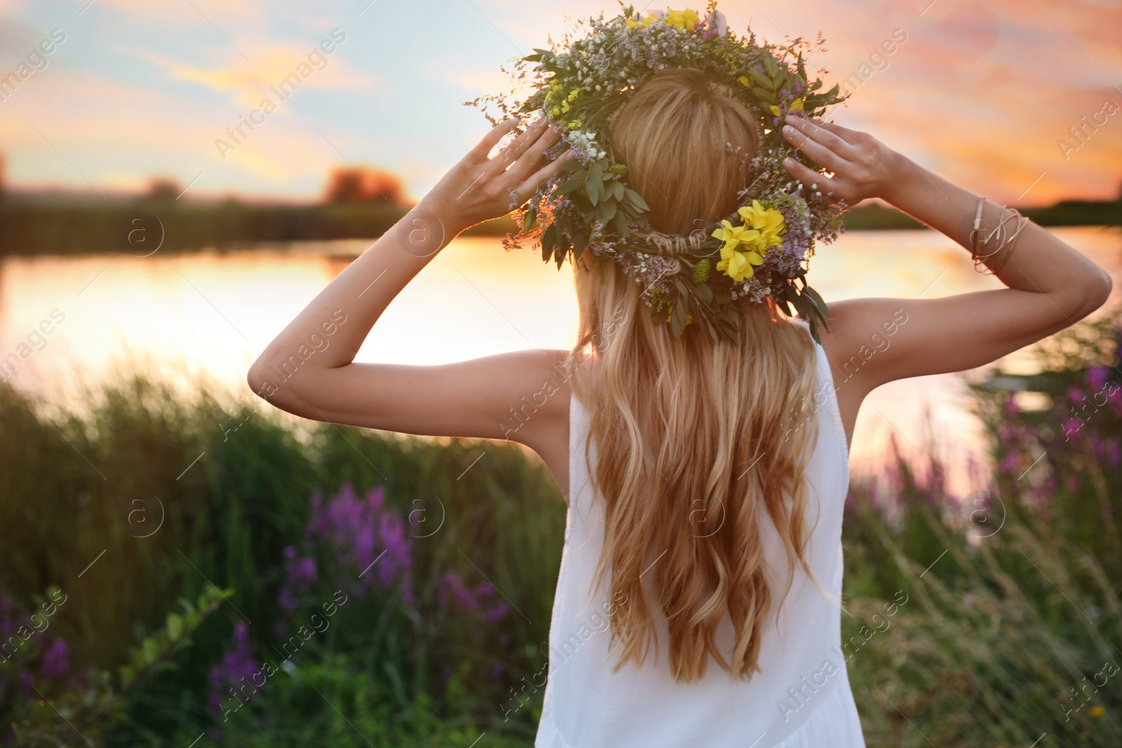 Photo of Young woman wearing wreath made of beautiful flowers outdoors at sunset