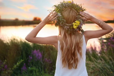 Young woman wearing wreath made of beautiful flowers outdoors at sunset